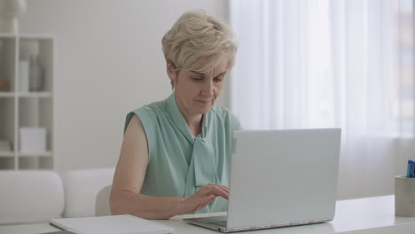 Una-Anciana-Contadora-Está-Trabajando-Con-Una-Computadora-Portátil-En-La-Oficina,-Una-Mujer-Está-Escribiendo-En-El-Teclado-Usando-Internet